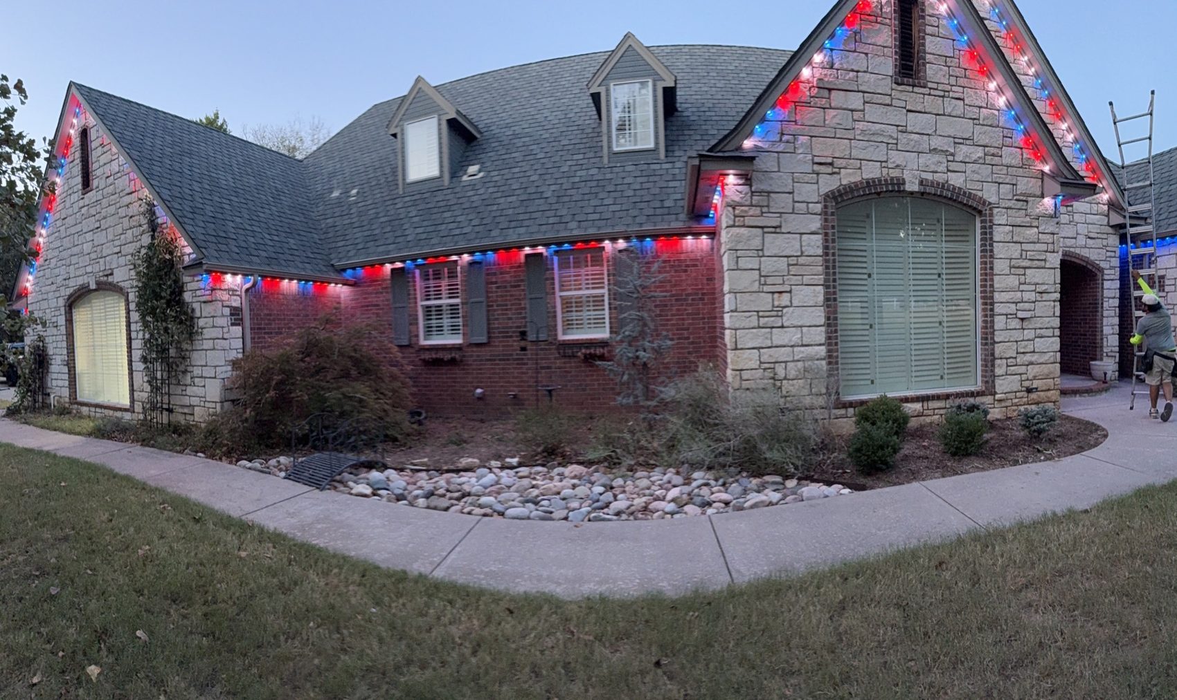 Brick home with red, white & blue permanent roofline lighting at dusk